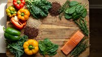 Fresh organic vegetables, salmon fillet, quinoa and herbs arranged on rustic wooden cutting board for healthy meal preparation and clean eating lifestyle.