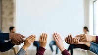 Diverse group of people joining hands together in circle, showing unity, teamwork, and collaboration in modern office environment with natural light.
