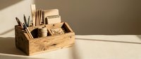 Wooden desk organizer with office supplies including pens, pencils, notebooks and stationery items on white surface with natural lighting for workspace organization.