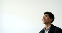 Young man with dark curly hair and medium brown skin tone wearing black blazer over light shirt, smiling while looking upward against white background for business and corporate use.