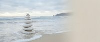 Zen stone stack balanced on sandy beach with gentle ocean waves and misty coastal mountains creating peaceful meditation atmosphere for wellness concepts.