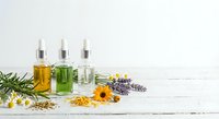 Essential oils in glass dropper bottles with natural herbs and flowers on white wooden background for aromatherapy and wellness treatments.