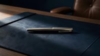 Luxury pen resting on dark leather notebook with wooden desk surface, executive office workspace for business writing and professional correspondence.