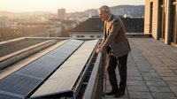 Senior male professional inspecting rooftop solar panels during golden hour with urban cityscape in background, renewable energy and sustainable business concept.