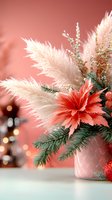 Festive winter arrangement with coral carnation, white pampas grass, and evergreen branches in ceramic vase against soft pink background with bokeh lights.