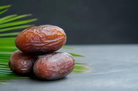 Fresh dates fruit arranged on palm leaf against dark background for healthy eating and Middle Eastern cuisine concepts.