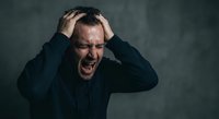 Stressed middle-aged Caucasian man holding head in hands screaming with emotional breakdown against dark background for mental health concepts.