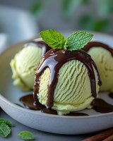 Pistachio ice cream scoops with chocolate sauce and fresh mint garnish on ceramic plate. Summer dessert for restaurant menus and food blogs.
