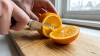 Close-up of hands slicing fresh orange on wooden cutting board near window, food preparation and healthy eating concept for culinary and kitchen design projects.