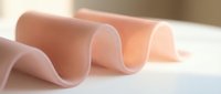 Rolled sheets of translucent pink material arranged on white surface, showcasing texture and light refraction for design, packaging, and product visualization projects.