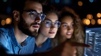 Three diverse software developers collaborating on coding project in modern office with computer screens and ambient lighting at night.