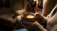 Hands holding warm beverage with lemon slice in cozy interior setting, perfect for lifestyle, wellness, comfort and seasonal content.