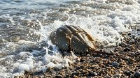 Ocean waves washing over smooth rocks on pebble beach shore with foamy white water and natural coastal scenery for relaxation and nature themes.