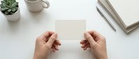 Female hands holding blank white card mockup on clean desk with succulent plant, coffee mug and wooden frame for branding design presentations.