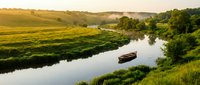 Peaceful river landscape with moored boat among lush green fields and trees at golden hour, suitable for travel and nature backgrounds.