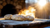 Fresh baked bread loaves on wooden board with steam rising and golden sunlight creating atmospheric bakery scene in morning light.