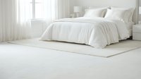 Serene bedroom interior with unmade white bed, cream bedding, and soft natural light from window with sheer curtains, suitable for home decor and lifestyle content.