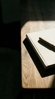 Blank notebook with pen on wooden desk surface illuminated by natural sunlight, suitable for writing, planning, journaling, and creative projects.