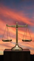 Golden scales of justice on wooden base against dramatic sunset sky with orange and purple clouds symbolizing legal balance and fairness.