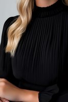 Young woman with blonde wavy hair wearing elegant black pleated turtleneck blouse, close-up fashion portrait on light background.