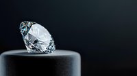 Brilliant cut diamond on dark pedestal against black background, luxury jewelry concept with dramatic lighting and reflective facets. Professional studio photography.
