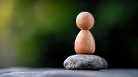 Minimalist wooden figure balancing on natural stone against blurred green background, representing zen, meditation, mindfulness and life balance.