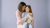 Loving mother embracing young daughter in tender moment. Caucasian woman and child sharing affectionate hug against soft purple background. Family bonding portrait.