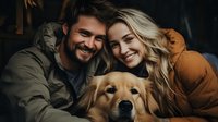 Young couple with golden retriever dog sharing intimate moment and genuine smiles in cozy dark setting, expressing joy and companionship in lifestyle portrait.