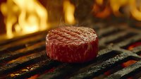 Juicy beef steak grilling on flaming barbecue grate with fire in background, close up view of medium rare meat cooking on hot grill surface.