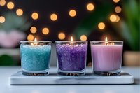 Aromatic scented candles in turquoise, purple, and pink with decorative crystals and salt, burning with warm bokeh lights background creating cozy atmosphere.