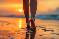 Barefoot woman walking on wet sandy beach at sunset with orange sun reflection on water, creating peaceful summer vacation atmosphere.