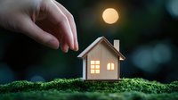Miniature wooden house with glowing windows on moss under full moon, creating magical atmosphere for real estate and home insurance concepts.