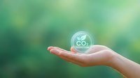 Hand holding transparent CO2 reduction bubble symbol against green nature background representing carbon footprint awareness and environmental sustainability.