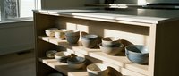 Modern kitchen display cabinet with open shelving showcasing ceramic dinnerware collection, bowls and plates in neutral tones, contemporary home decor and tableware storage solution.