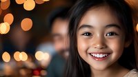 Young Asian girl with bright genuine smile against blurred warm bokeh lights background, radiating happiness and joy in natural portrait setting.