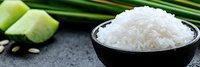 Steamed jasmine rice in black ceramic bowl with fresh lime wedges and green onion on dark stone background. Asian cuisine ingredients.