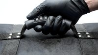 Professional mechanic in black gloves using specialized tool for automotive repair work on textured surface component maintenance.