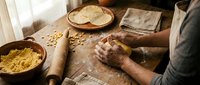 Traditional pasta making process with fresh egg noodles being hand-rolled on wooden surface. Artisan chef preparing homemade Italian cuisine in rustic kitchen setting.
