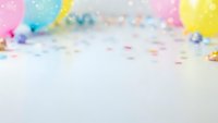 Colorful birthday party balloons and confetti scattered on white surface creating festive celebration background with copy space for text and design.
