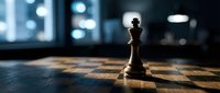 Chess king piece standing alone on wooden chessboard in modern office with blurred city lights background symbolizing leadership and strategic thinking.