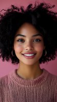 Young African American woman with natural curly afro hair and bright smile wearing pink sweater against pink background, perfect for beauty and lifestyle content.