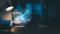 Businessman holding smartphone displaying glowing upward trending arrow chart with financial data analytics and growth statistics for business success and investment strategy.
