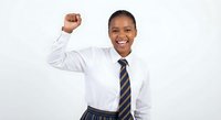 Happy African American businesswoman celebrating success with raised fist gesture wearing white shirt and striped tie on light background.