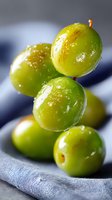Fresh green grapes with water drops on gray linen cloth background, macro shot showing juicy texture and natural shine in soft lighting.