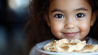 Young mixed-race girl enjoying homemade waffles with syrup at breakfast table. Child eating sweet morning meal with happy expression and messy face.