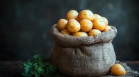 Fresh raw potatoes in rustic burlap sack on dark background with green herbs, moody food photography for farm market and organic produce advertising.