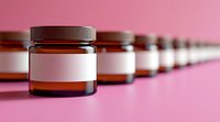 Row of amber glass cosmetic jars with blank white labels on pink background, selective focus on front jar, fading perspective line for product mockup and branding.
