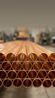 Stack of shiny copper pipes arranged in rows at industrial warehouse facility for plumbing construction and manufacturing applications.