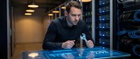Focused Caucasian male IT specialist analyzing holographic data interface in modern server room with network equipment and blue lighting technology.