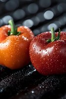 Fresh ripe tomatoes with water drops on dark background, macro shot showing detailed texture and natural moisture for food photography and marketing.